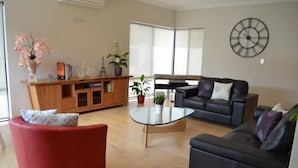 Una sala de estar moderna con una mesa de centro de vidrio, dos sofás, un sillón rojo y un mueble de madera con objetos decorativos.