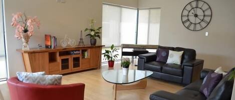 A modern living room with a glass coffee table, two sofas, a red armchair, and a wooden cabinet with decorative items.