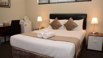 A neatly made hotel room with a large bed, two bedside lamps, a small desk with a coffee maker, and a nightstand with a lamp.