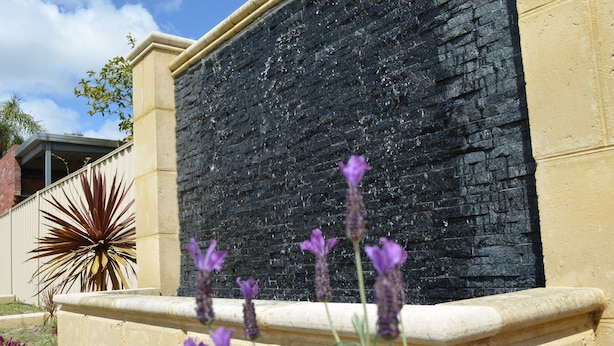 Muro de piedra con flores moradas al frente.