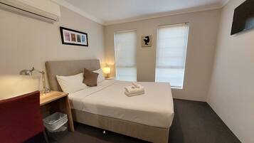 Una habitación de hotel con cama, mesita de noche, lámpara y un cuadro en la pared.
