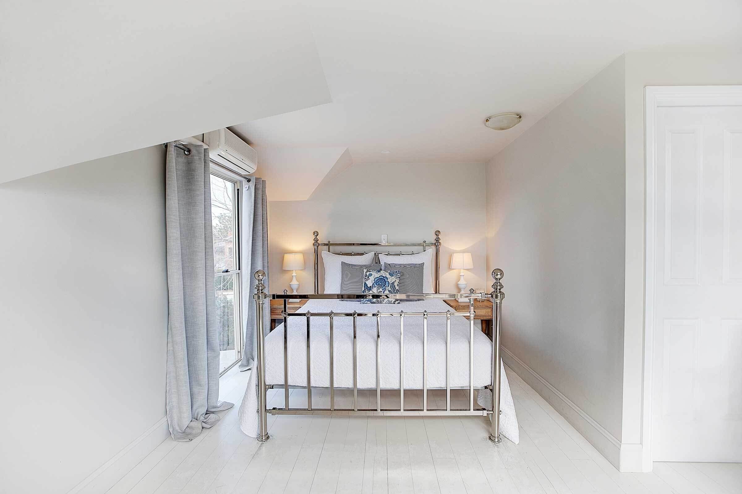 A bedroom with a bed, bedside lamps, and a window with curtains.