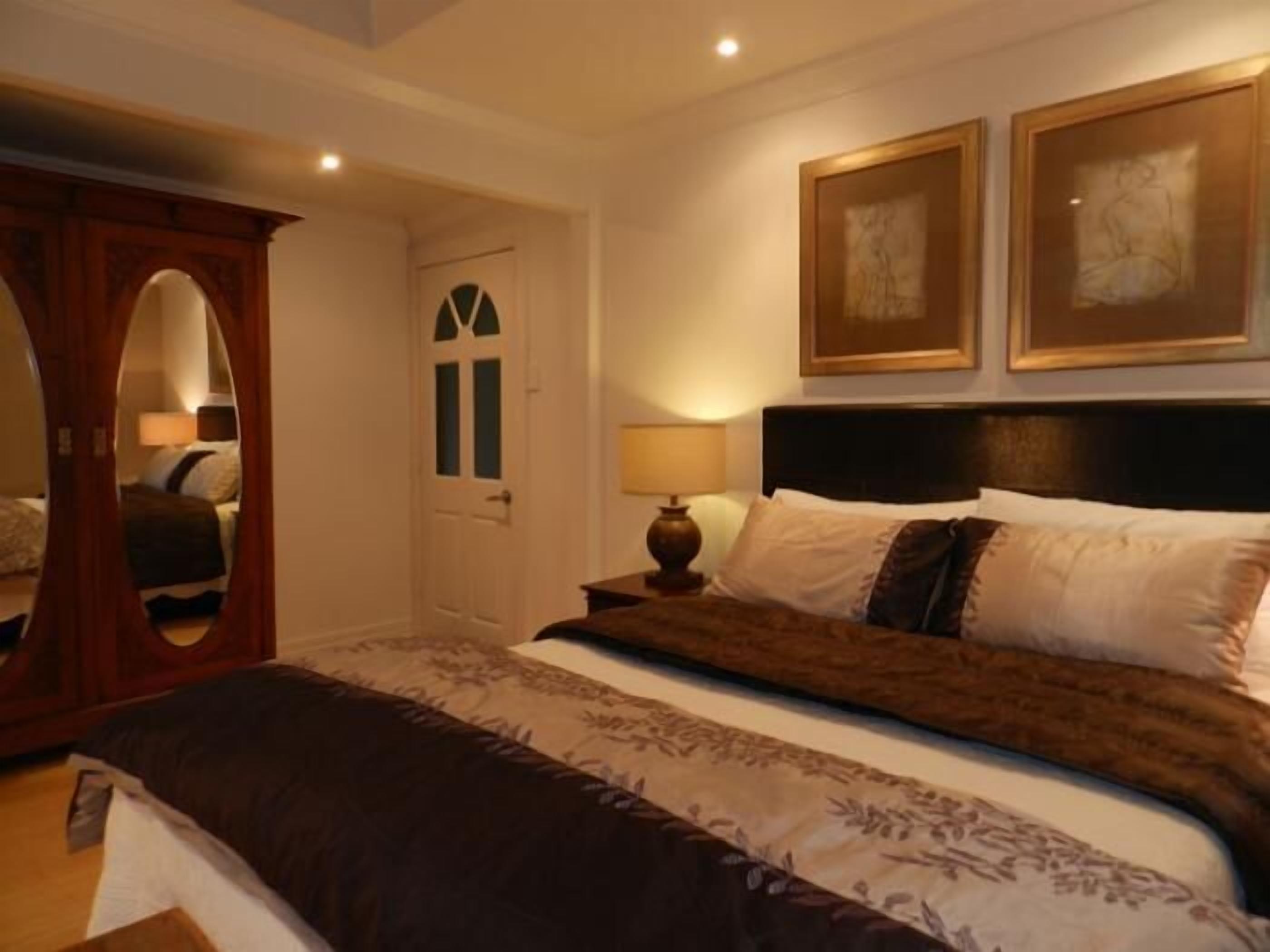 A bedroom with a large bed, a wooden wardrobe, and two framed artworks on the wall.