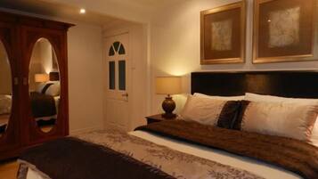 A bedroom with a large bed, a wooden wardrobe, and two framed artworks on the wall.