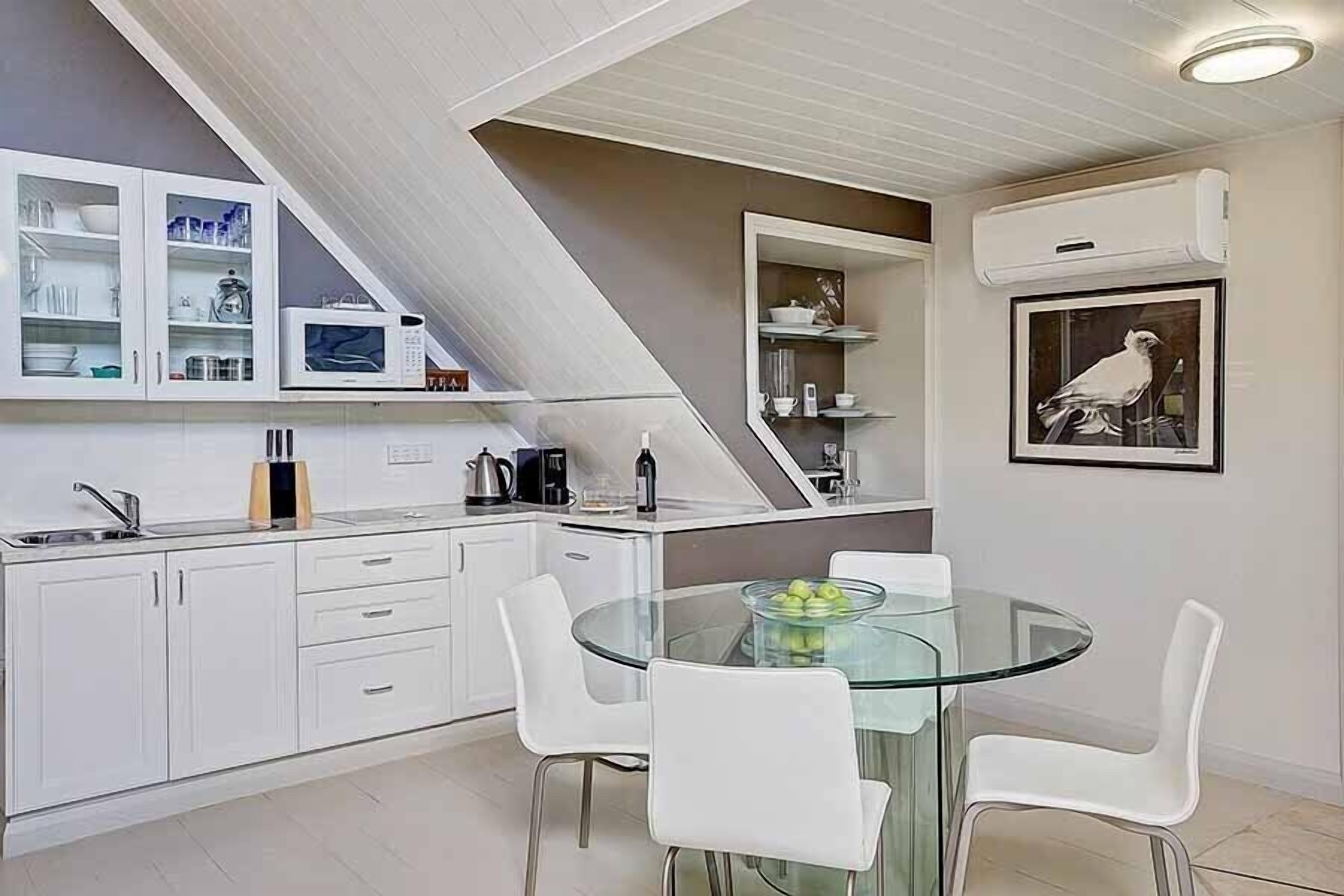 A modern kitchen with white cabinets, a glass dining table, and white chairs.