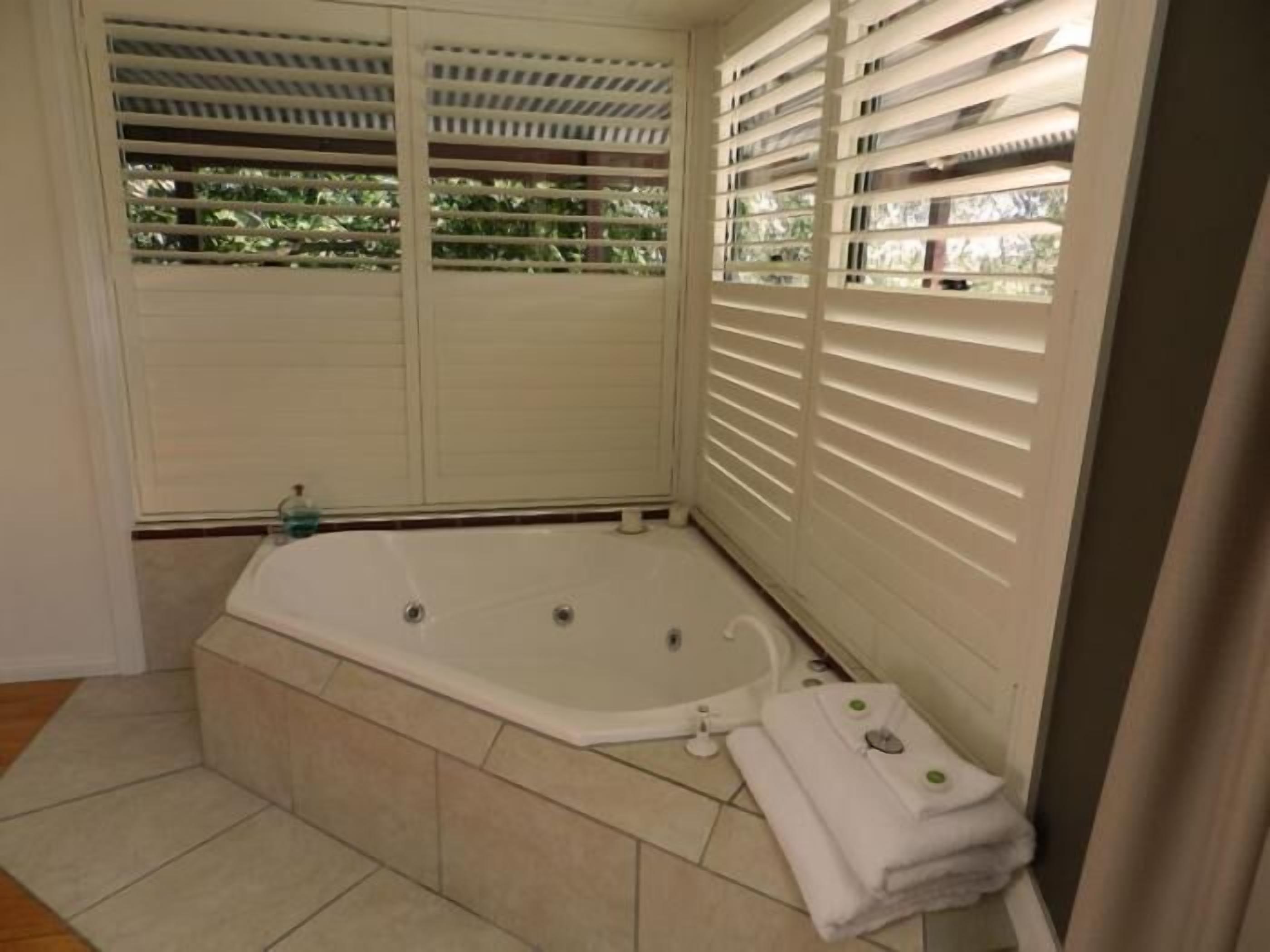 Une salle de bain avec une baignoire, une douche et une fenêtre équipée de stores.