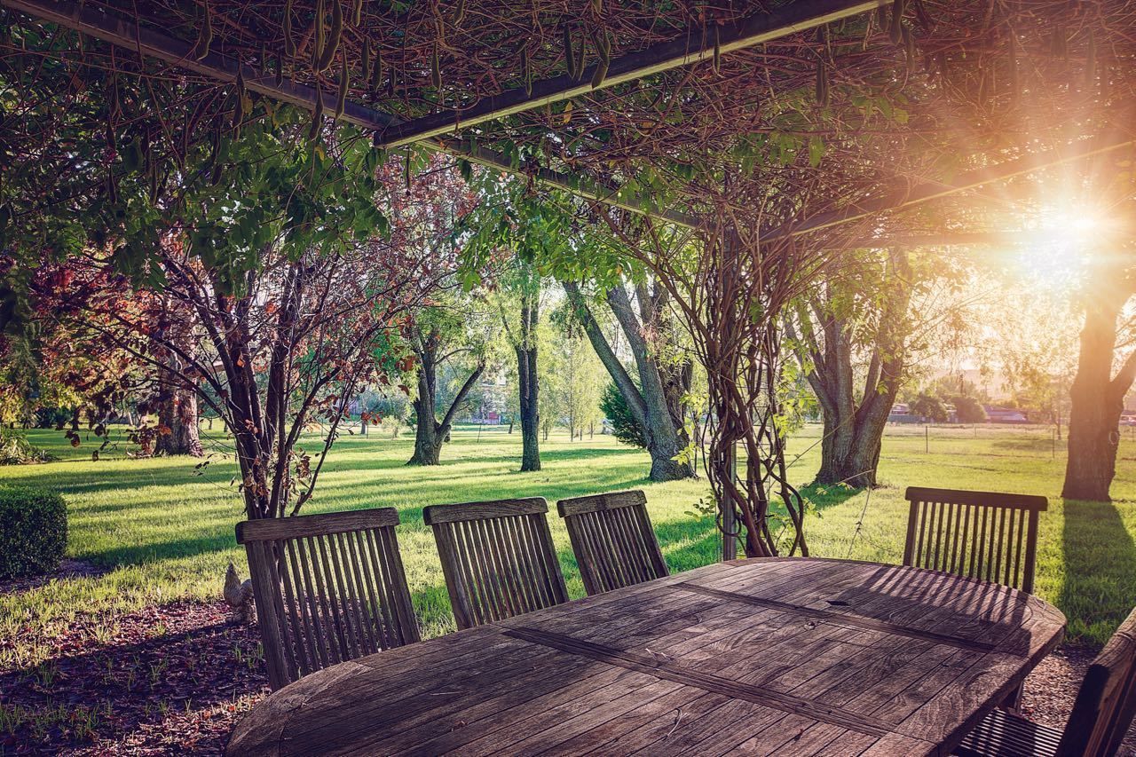 A wooden table and chairs set outdoors with a view of a grassy park and trees.