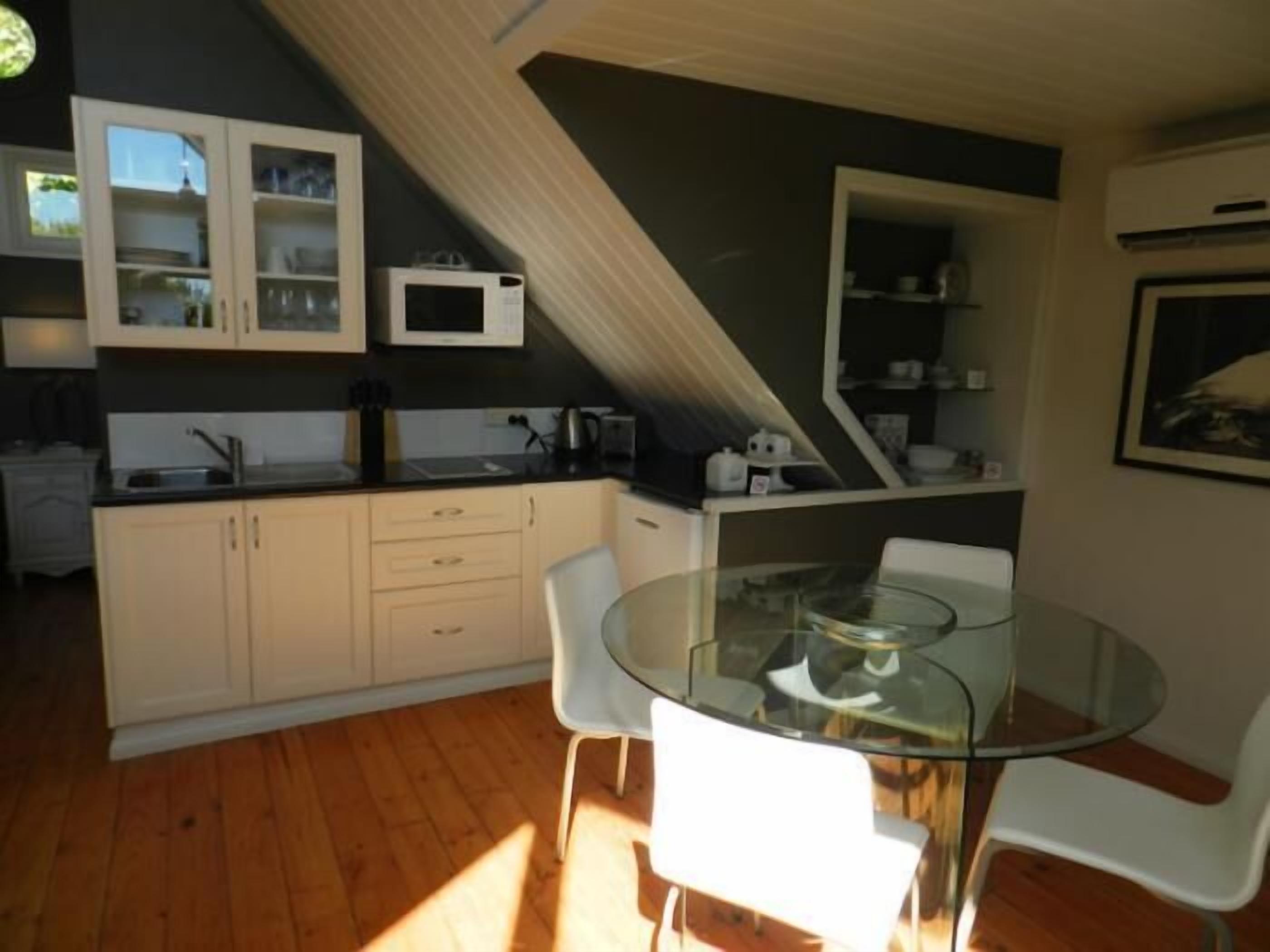 Una cocina moderna con armarios blancos, una mesa de comedor de vidrio y una silla blanca.