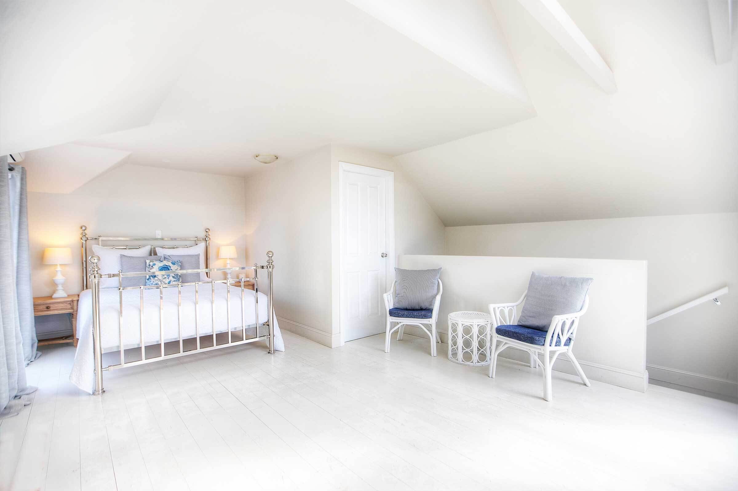 A bedroom with a bed, two chairs, a small table, and a door.