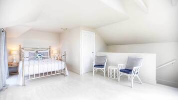 A bedroom with a bed, two chairs, a small table, and a door.