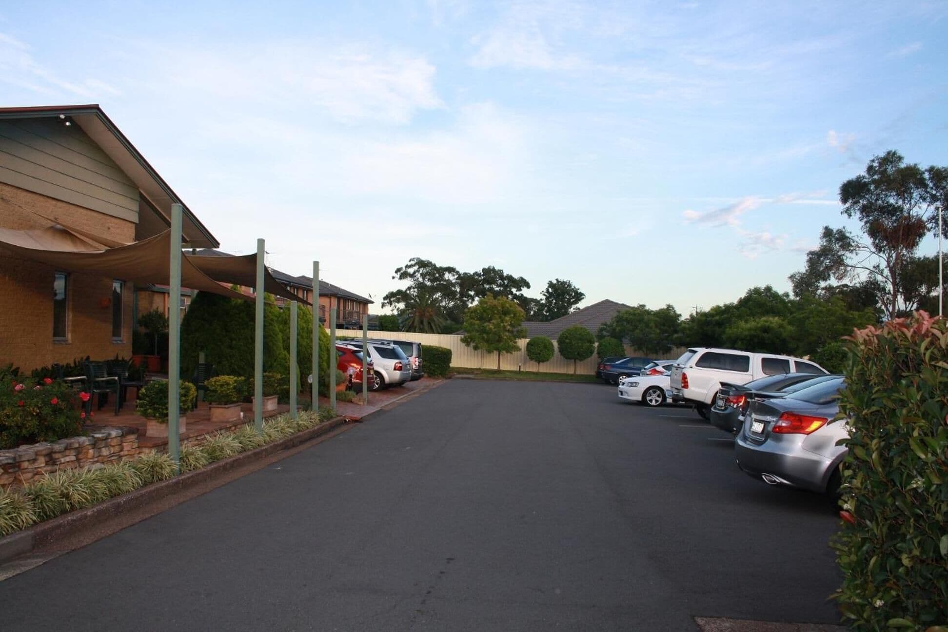 A parking lot with several cars parked, a building with a covered patio area, and a clear sky.