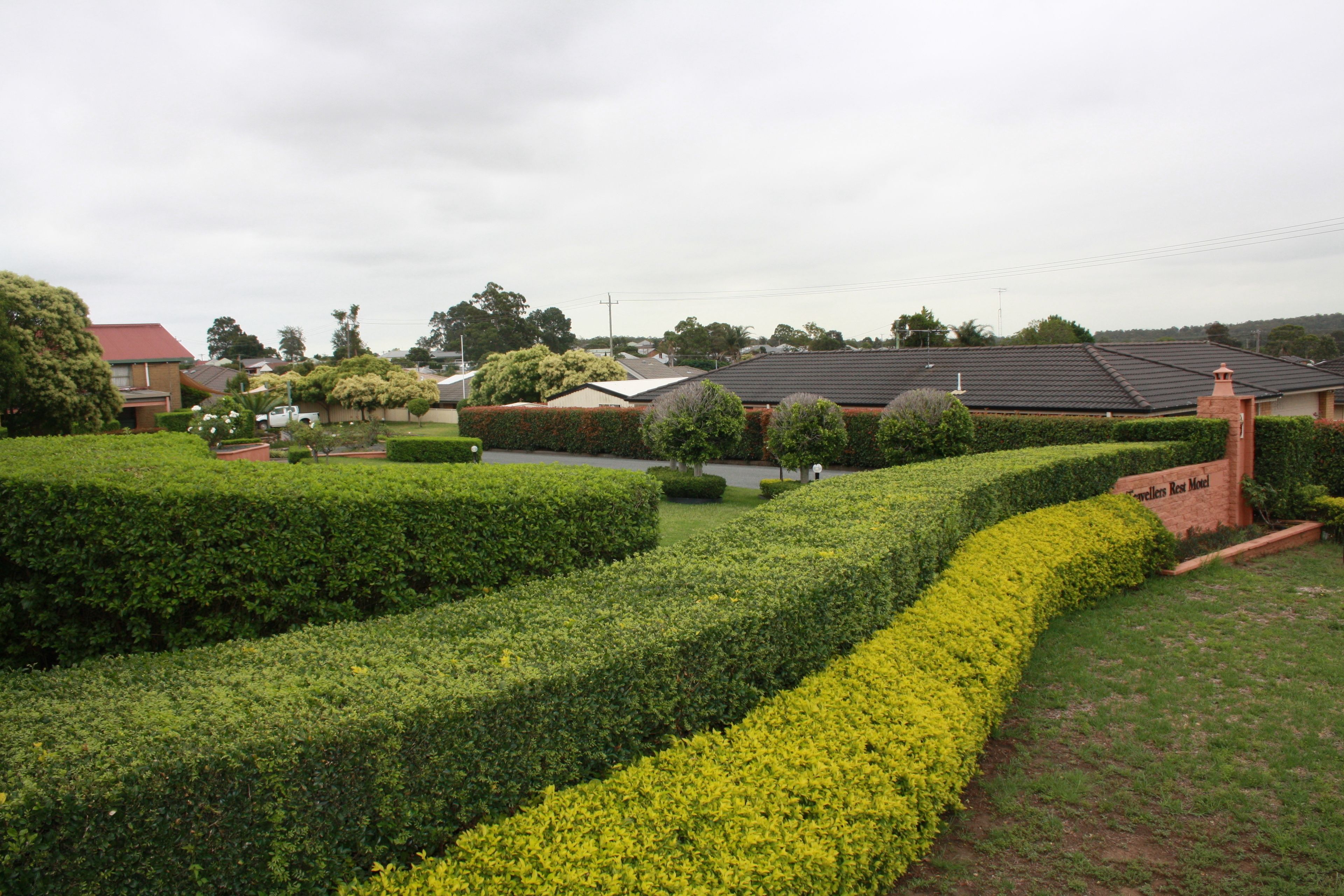 A residential area with neatly trimmed hedges, a well-maintained lawn, and a brick building with a sign that reads "Glenferrie Rest Motel".