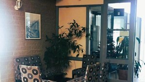 Un comedor con una mesa redonda y sillas estampadas, una planta en maceta y una pared de ladrillo con un cuadro enmarcado.