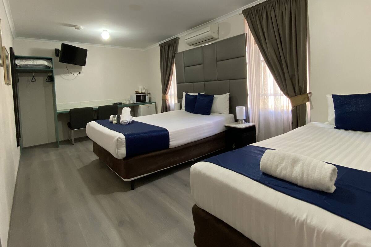 A hotel room with two beds, a desk, a television, and an air conditioning unit.