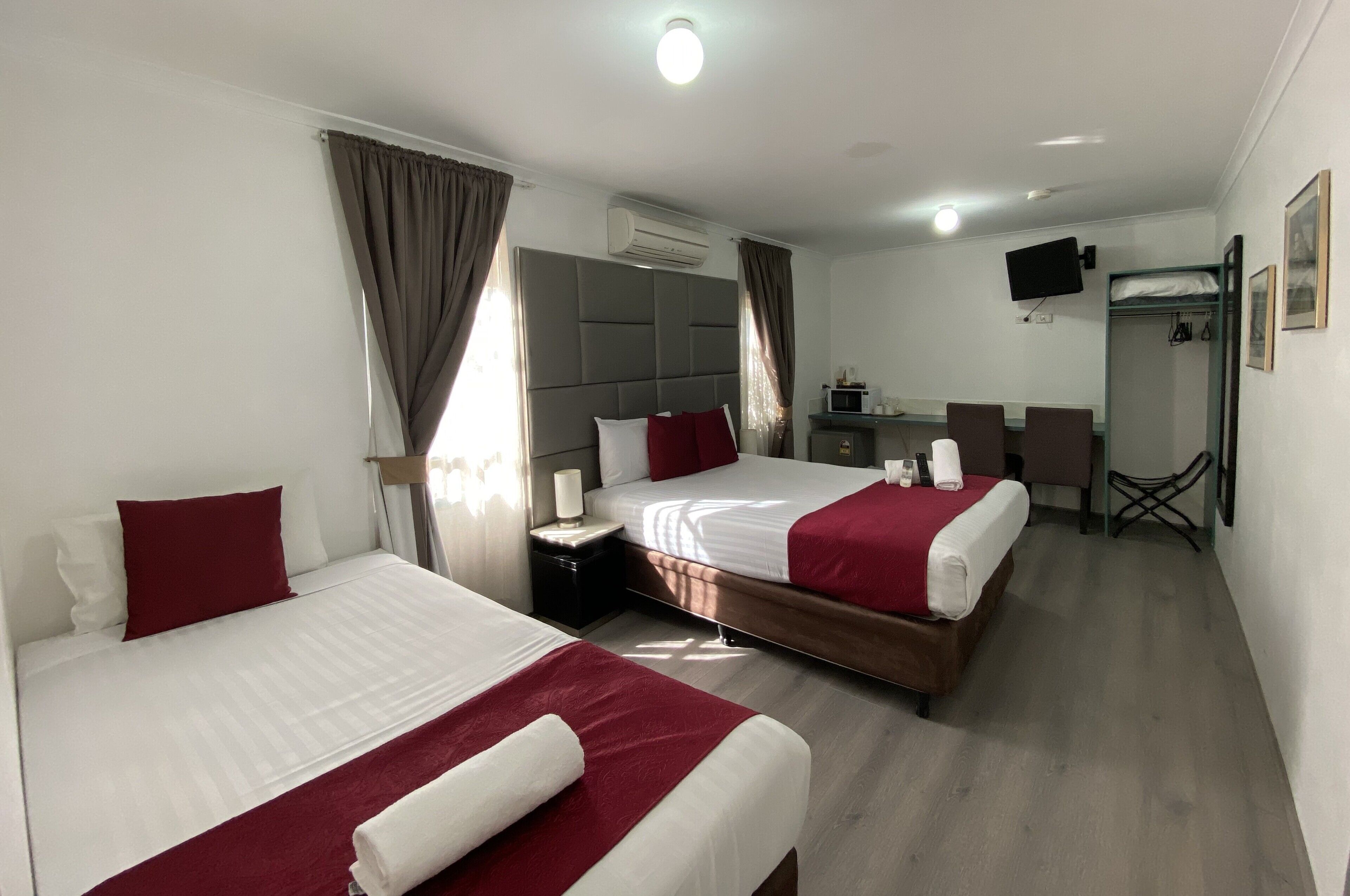 A hotel room with two beds, a desk, a chair, an air conditioning unit, and a television.