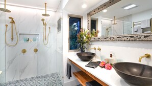 A modern bathroom with a large mirror, a black vessel sink, a shower with gold fixtures, and a patterned floor. - Lovestone Cottages (Montville)