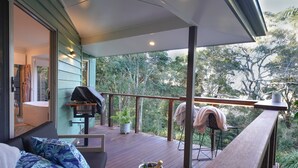 A covered outdoor deck with a barbecue grill, seating area, and a view of the surrounding greenery. - Lovestone Cottages (Montville)