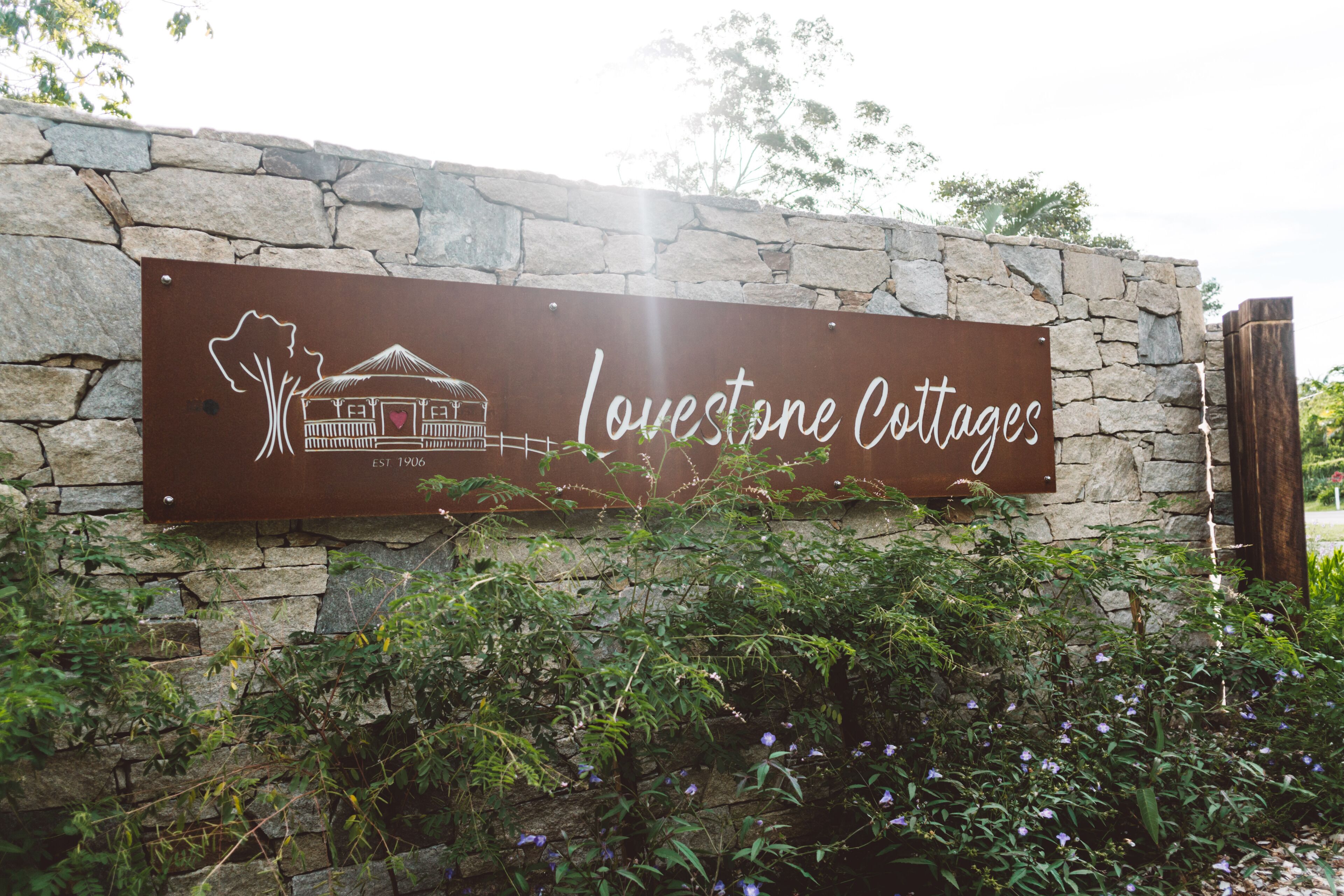 Een bordje voor Lovestone Cottages, met een stenen muur en begroeiing ervoor.