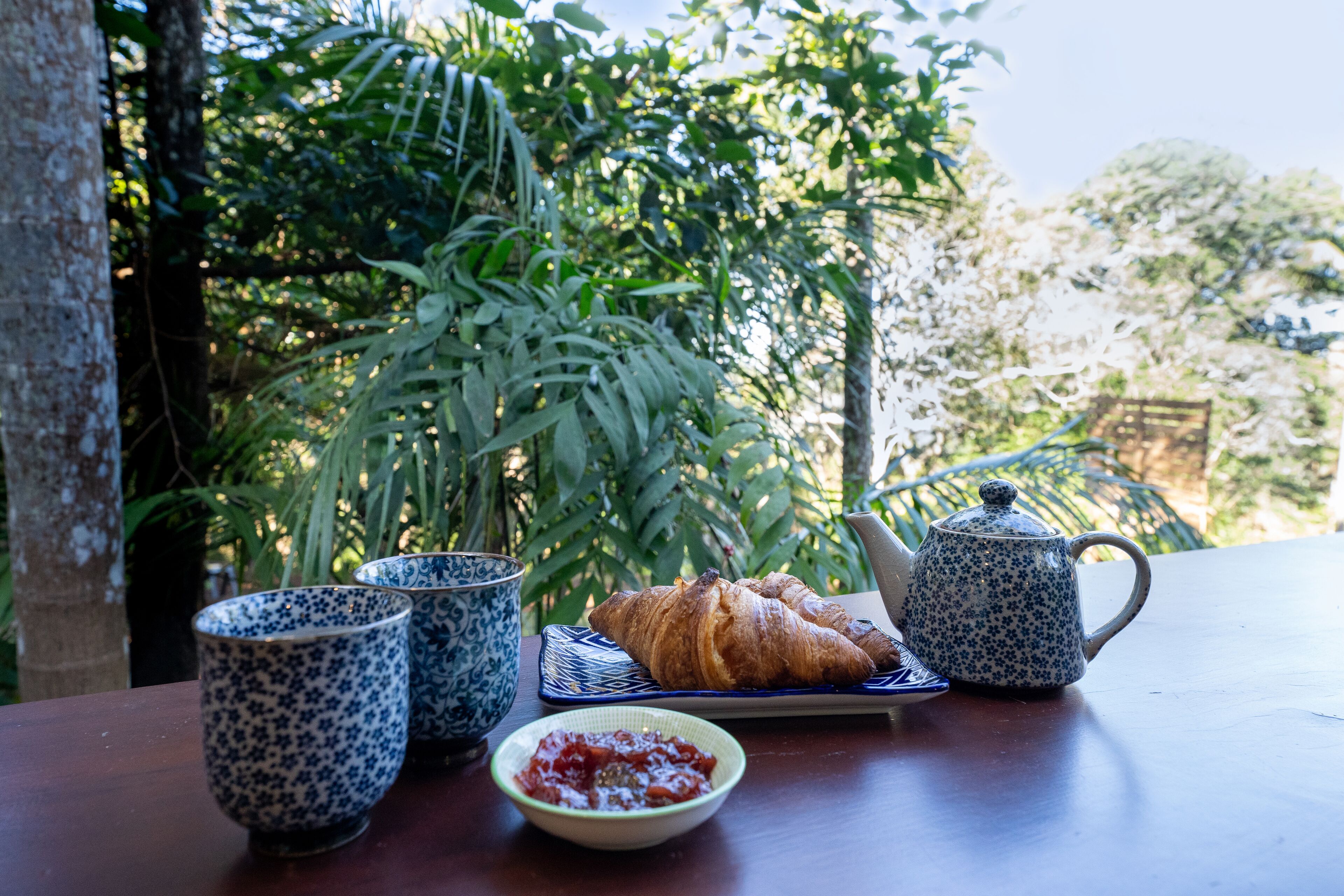 Une table avec un croissant, un bol de confiture et deux tasses à motifs.