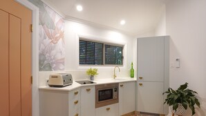 A compact kitchen with a toaster, sink, microwave, and a window with blinds. - Lovestone Cottages (Montville)