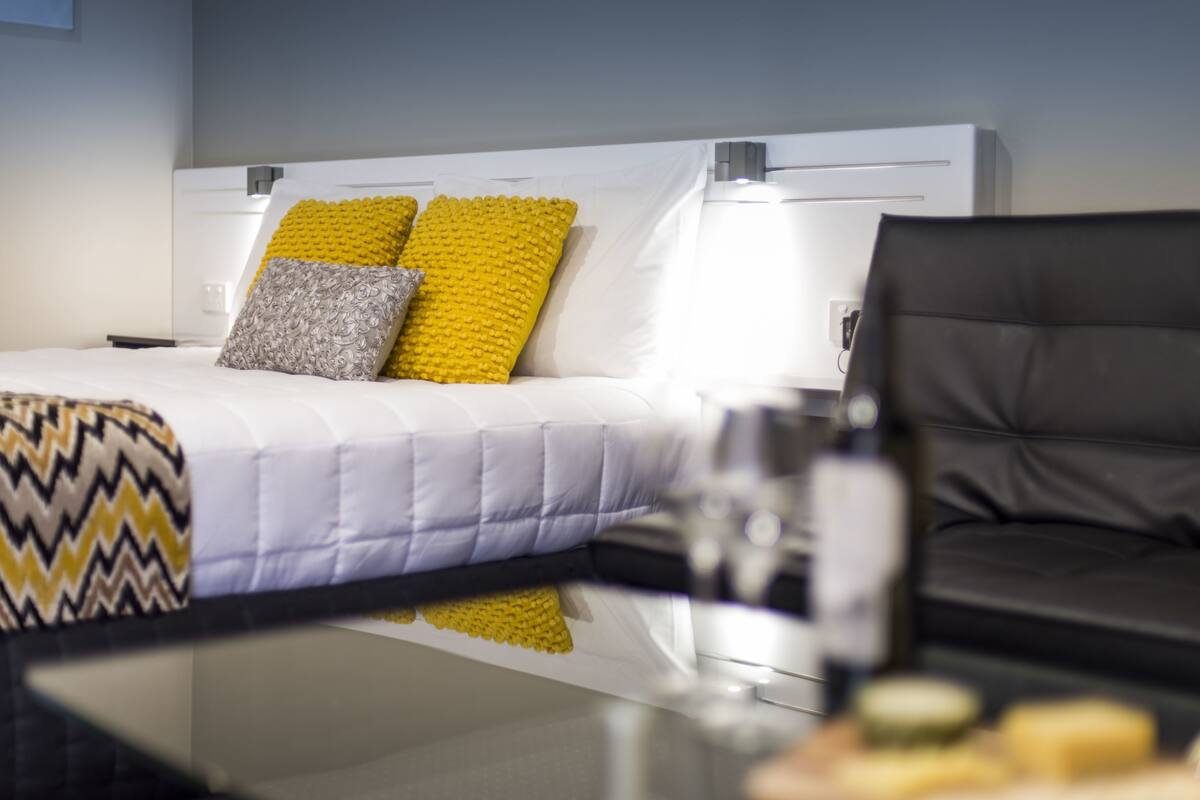 A modern hotel room with a neatly made bed, a black leather sofa, and a glass table.