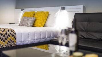 Una habitación de hotel moderna con una cama bien hecha, un sofá de cuero negro y una mesa de vidrio.
