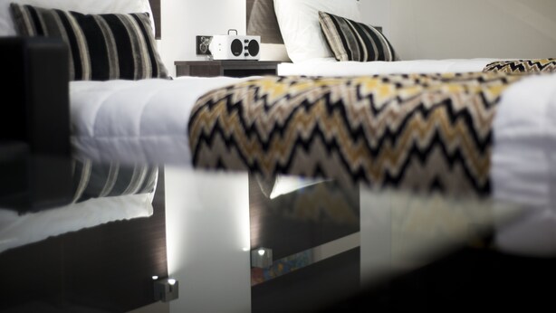 A modern hotel room with a neatly made bed, a bedside table with a radio, and a nightstand.