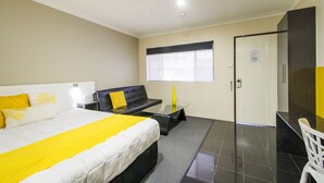A hotel room with a bed, a black sofa, a glass table, and a desk.