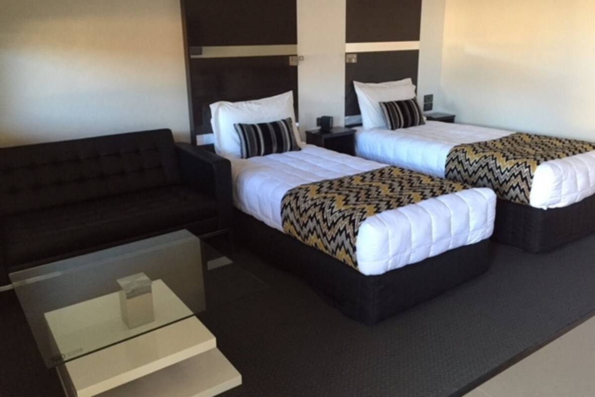 A hotel room with two beds, a sofa, and a glass coffee table.