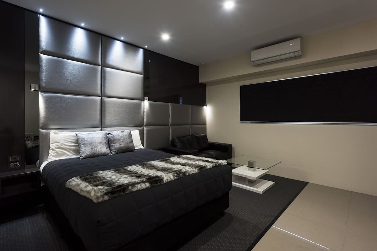 A modern bedroom with a large bed, a glass side table, and a mounted TV.