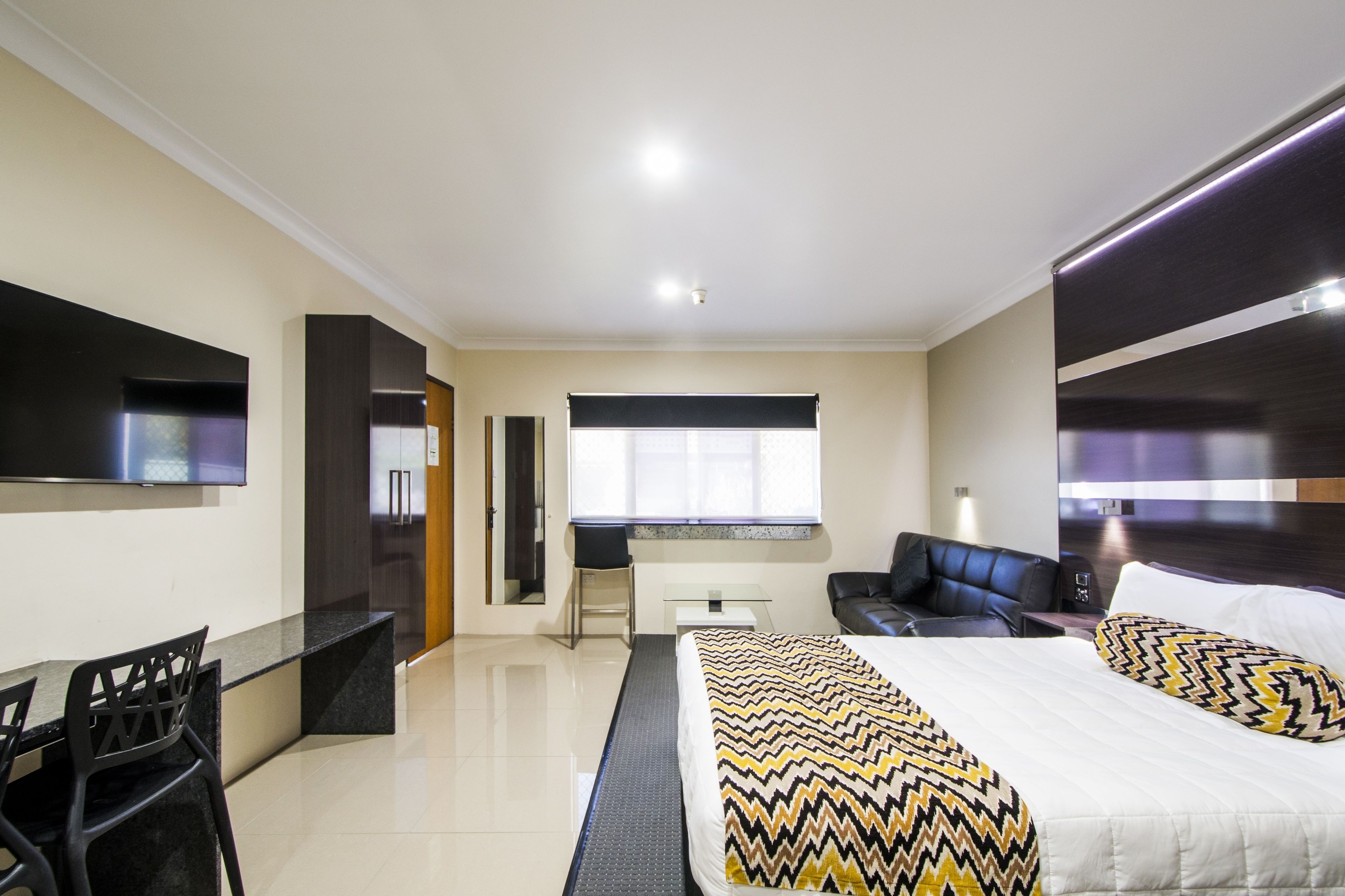 Una habitación de hotel moderna con una cama, un escritorio, una silla, un sofá y un televisor.