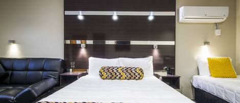 Una habitación de hotel con una cama grande, un sofá de cuero negro, una mesita de noche, aire acondicionado y un aplique de pared.