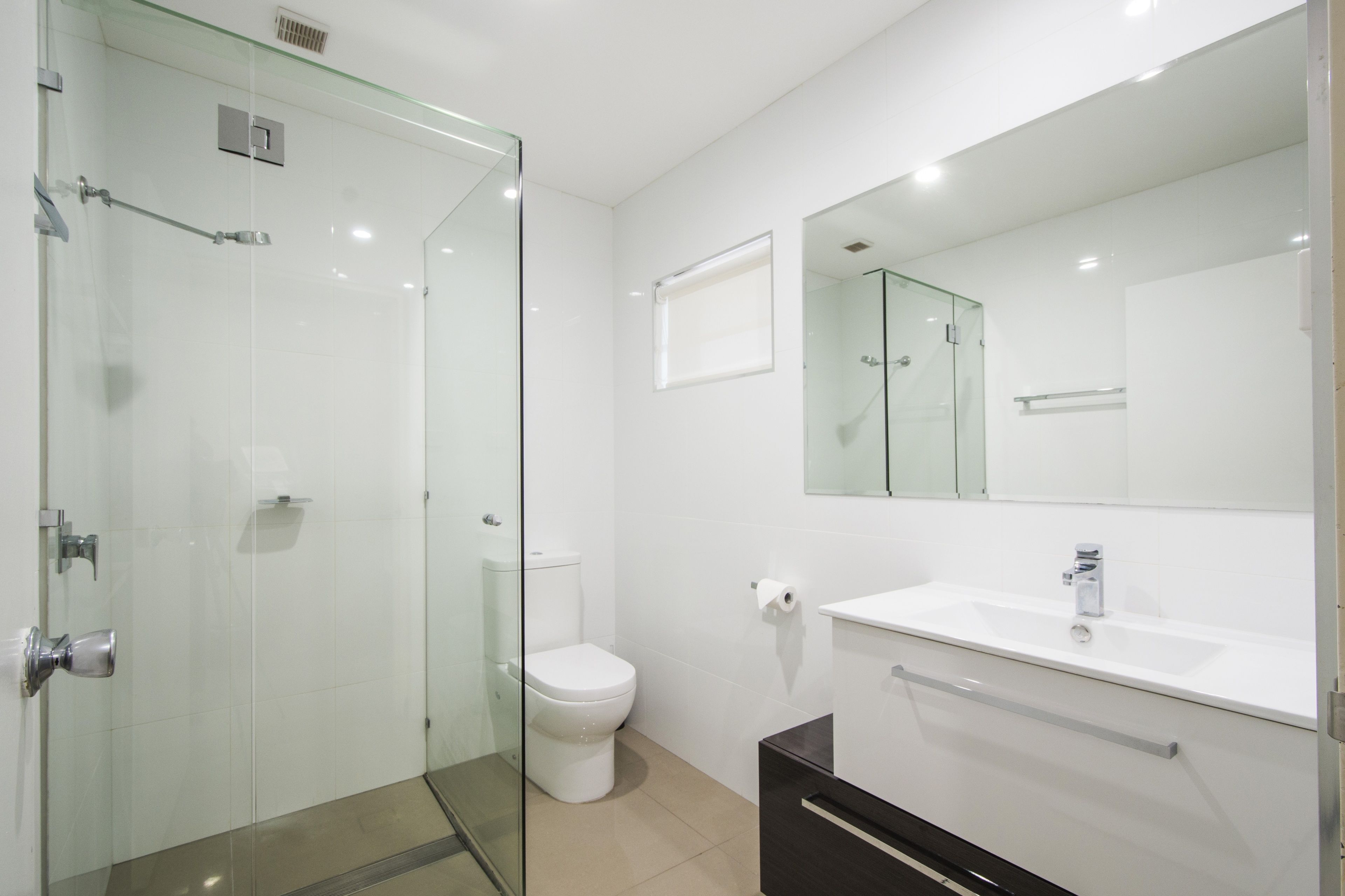 Een moderne badkamer met een douchecabine van glas, een wit toilet, een wastafel met spiegel erboven en een donkere kast eronder.