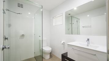 Een moderne badkamer met een douchecabine van glas, een wit toilet, een wastafel met spiegel erboven en een donkere kast eronder.