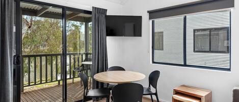 Una habitación moderna con una puerta corrediza de vidrio que da a una terraza, una mesa redonda de madera con sillas y una pequeña mesita de madera.