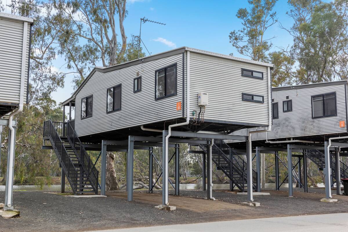 Conjunto de edificios modulares elevados con escaleras exteriores, rodeado de árboles y un cielo despejado.