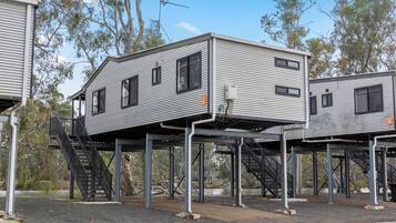 Conjunto de edificios modulares elevados con escaleras exteriores, rodeado de árboles y un cielo despejado.
