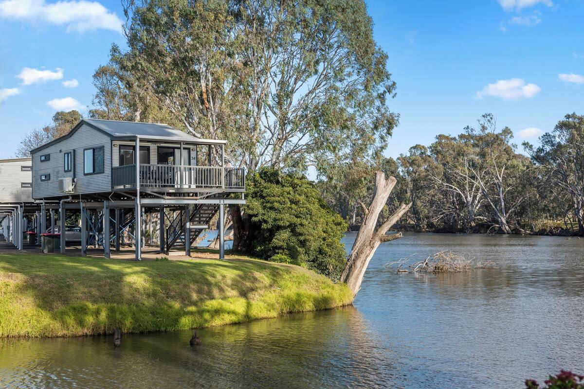Una casa de dos pisos con un balcón que da a un lago, rodeada de árboles.