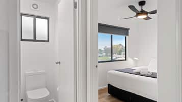 A modern bedroom with a bed, a window with a view, a ceiling fan, and a white toilet.