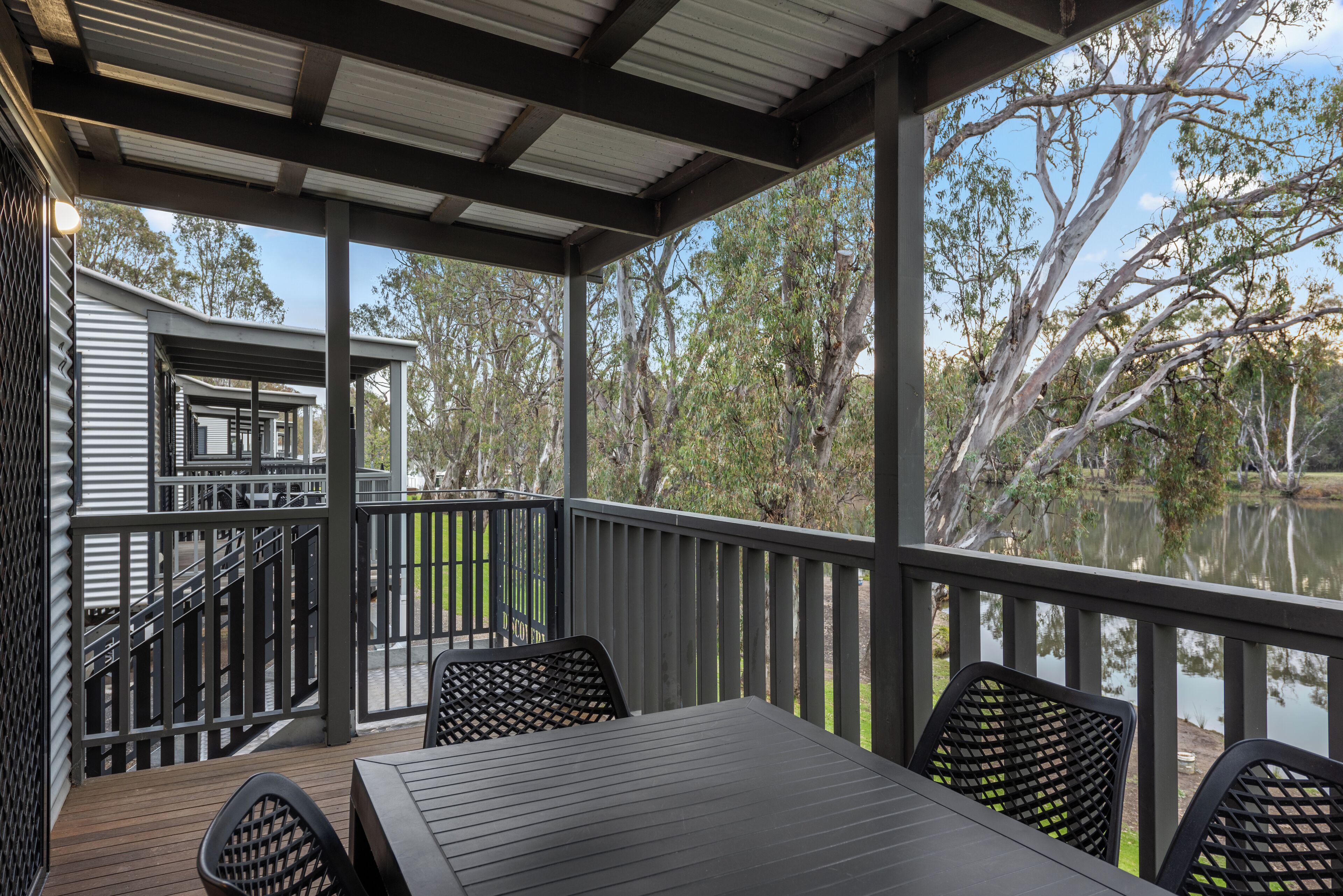 A covered outdoor deck with a table and chairs, overlooking a body of water and trees.
