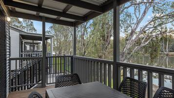 A covered outdoor deck with a table and chairs, overlooking a body of water and trees.