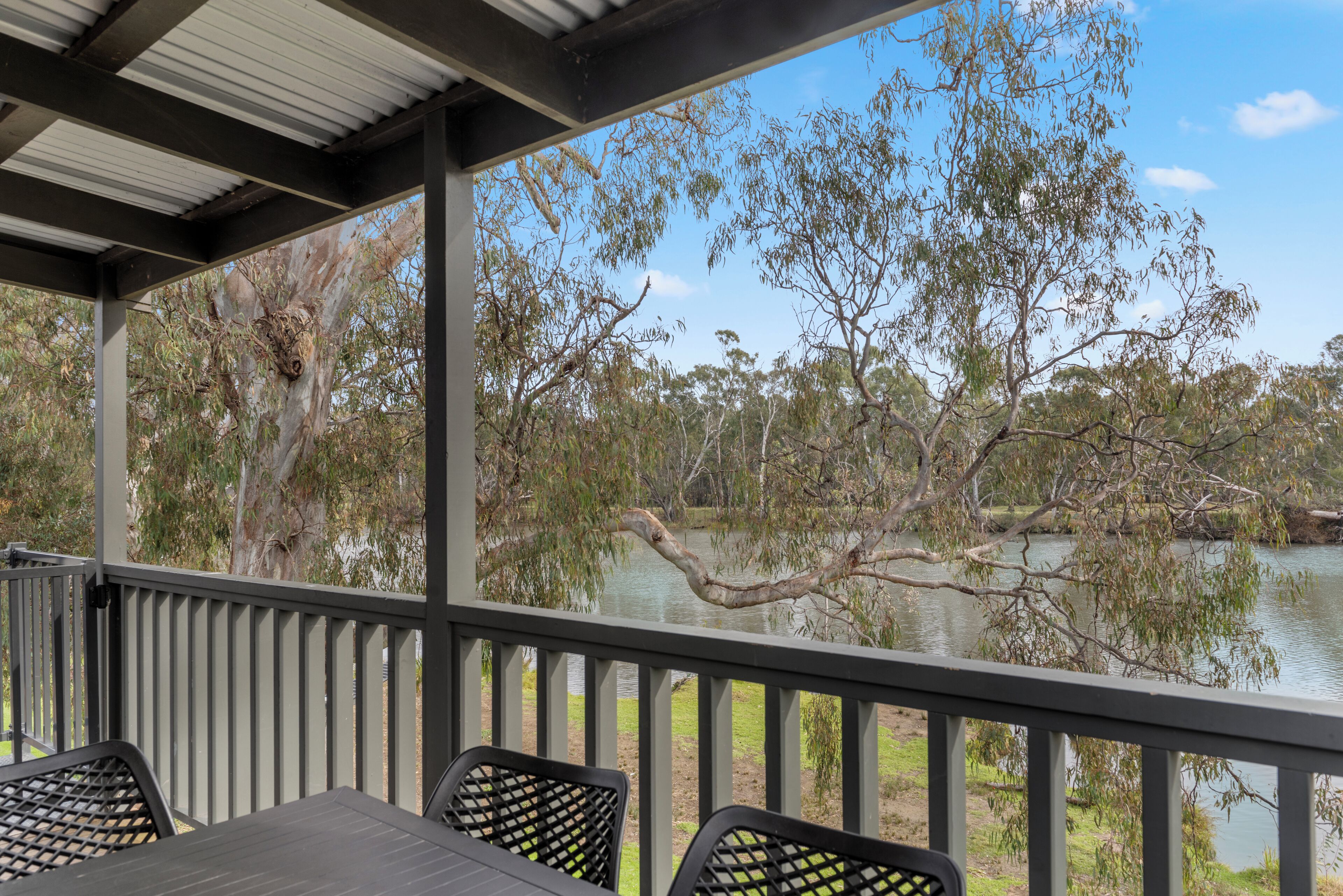 A covered outdoor area with a table and chairs, overlooking a calm lake and trees.
