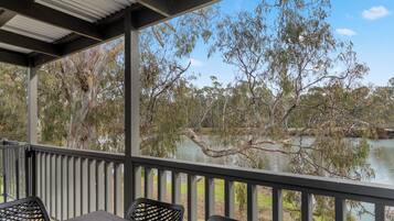 A covered outdoor area with a table and chairs, overlooking a calm lake and trees.