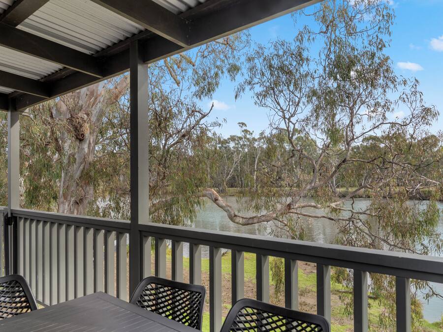 A covered outdoor area with a table and chairs, overlooking a calm lake and trees.