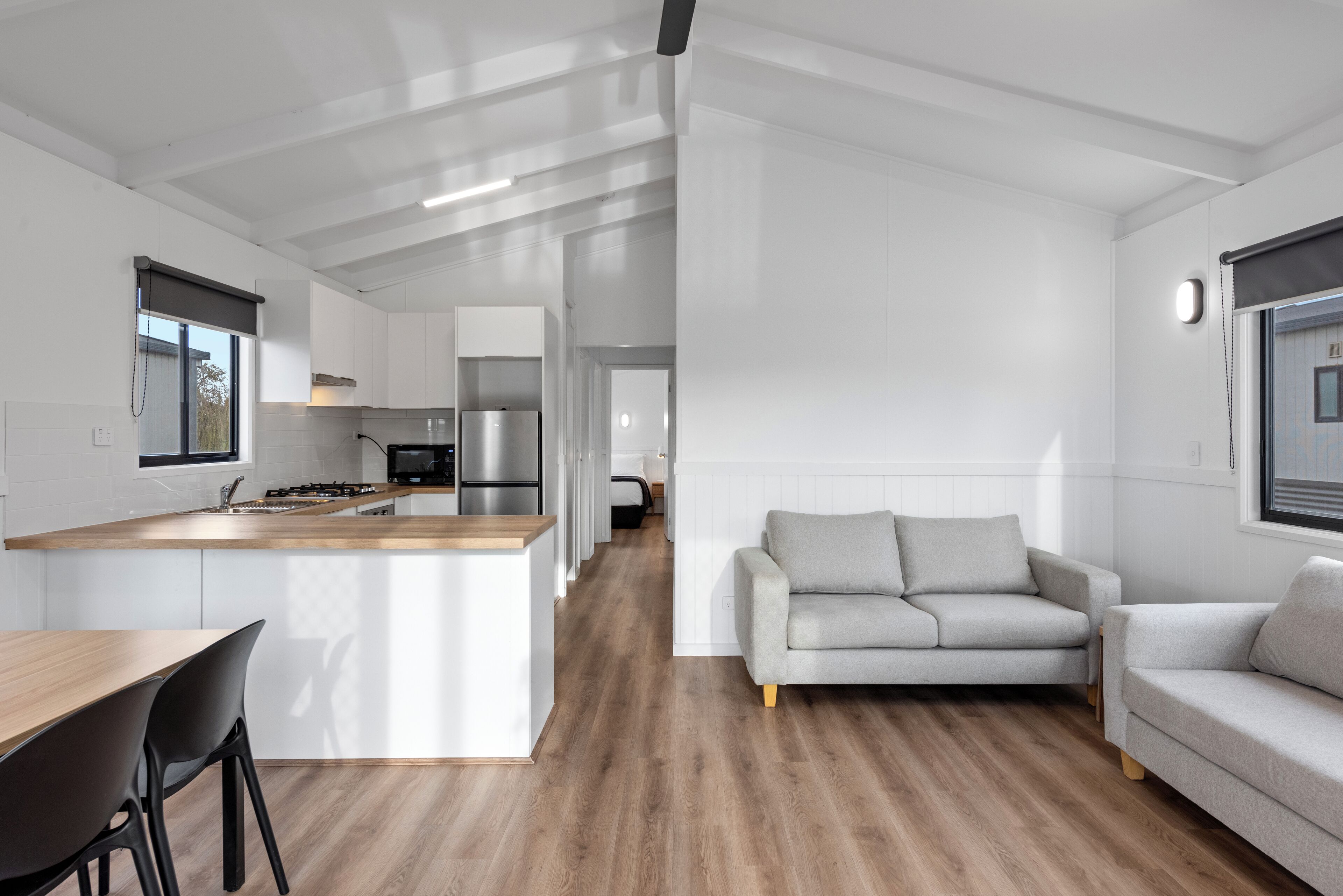 Una cocina moderna con una isla central, un comedor con mesa y sillas de madera, y una sala de estar con un sofá gris y otro sofá.