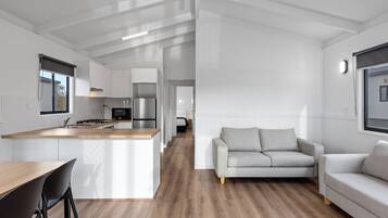 Una cocina moderna con una isla central, un comedor con mesa y sillas de madera, y una sala de estar con un sofá gris y otro sofá.