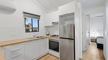 A modern kitchen with white cabinets, a stainless steel refrigerator, a built-in oven, and a window with blinds.