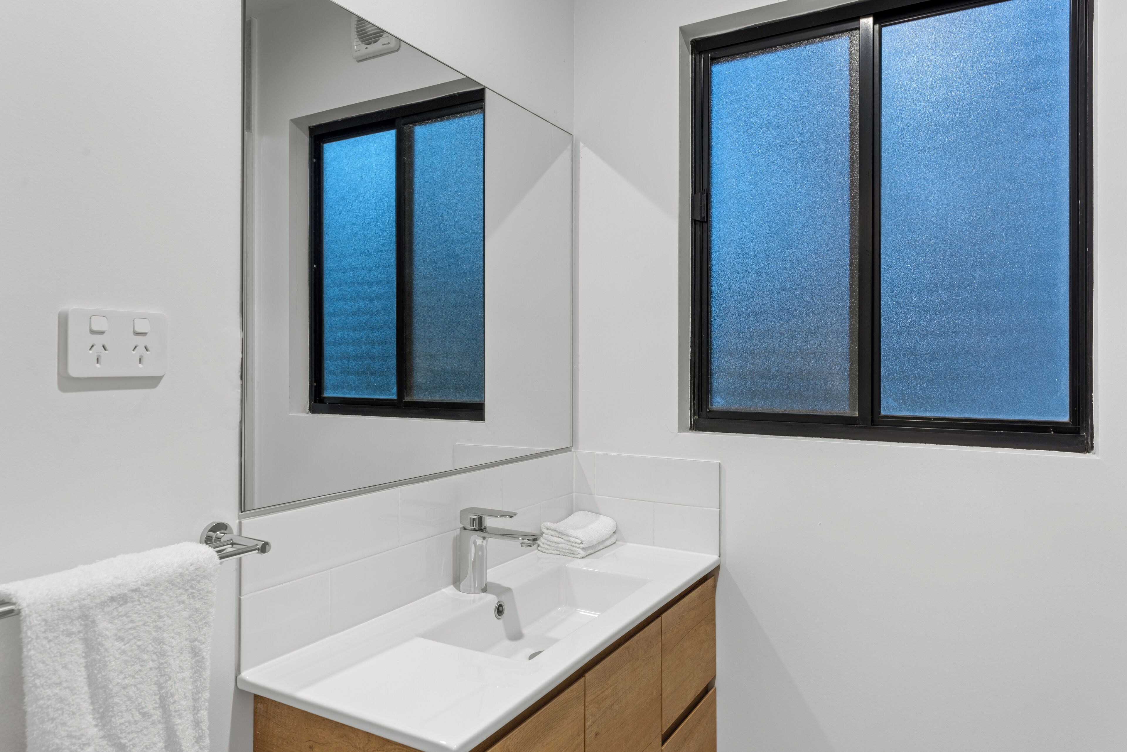 Une salle de bain moderne avec un lavabo blanc, un miroir et une fenêtre.