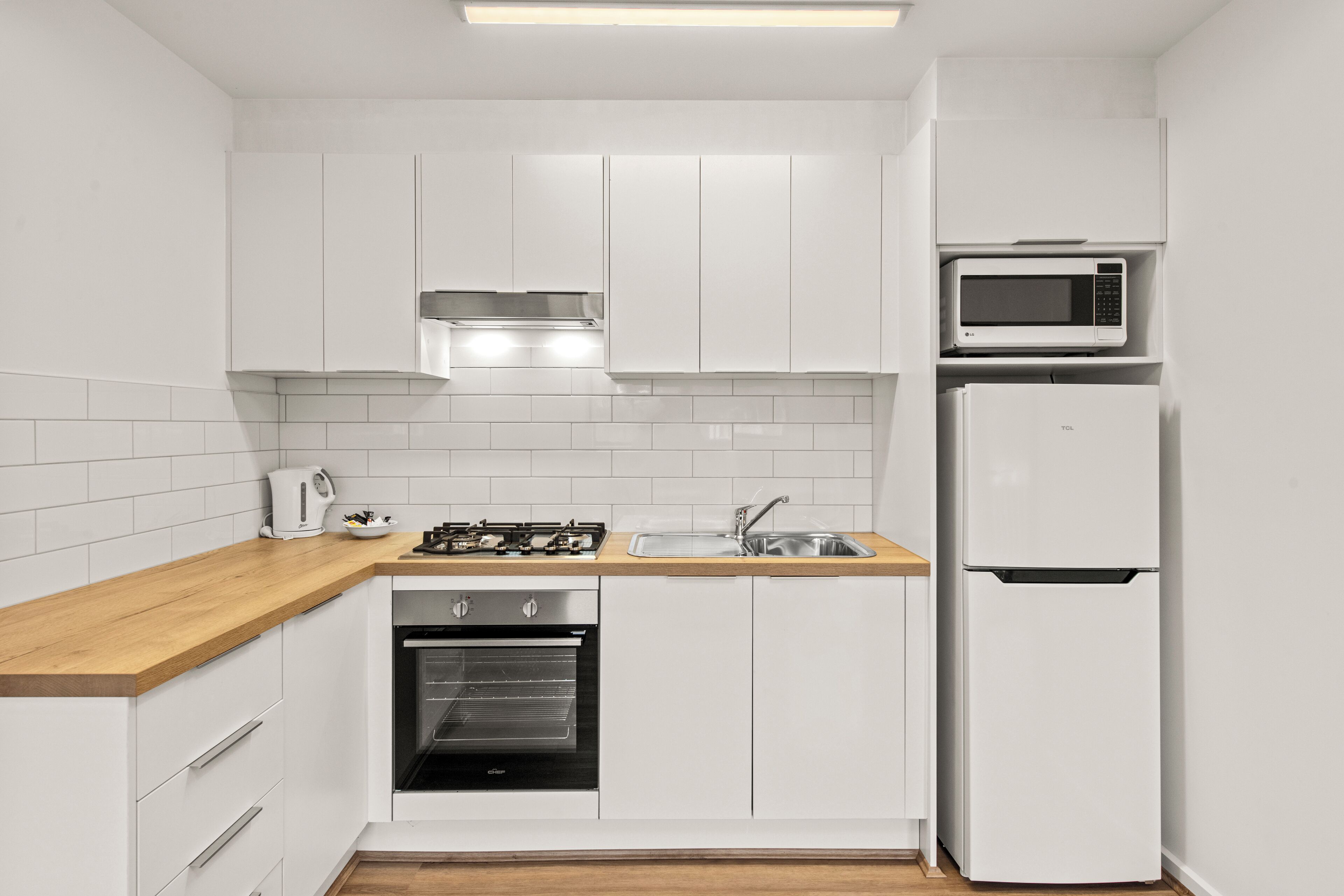 A compact kitchen with white cabinets, a wooden countertop, a built-in oven, a microwave, and a refrigerator.