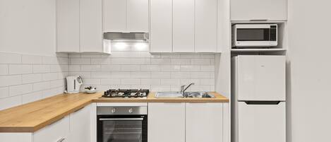 A compact kitchen with white cabinets, a wooden countertop, a built-in oven, a microwave, and a refrigerator.
